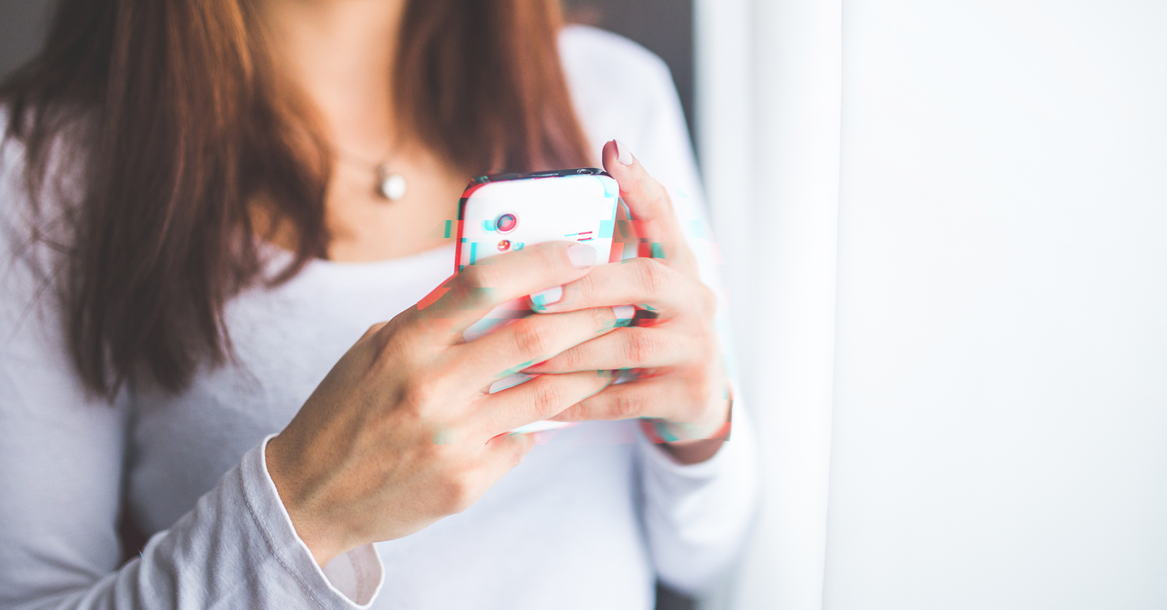 “A woman with shoulder-length brown hair wearing a white sweater, holding a smartphone in her hand.”