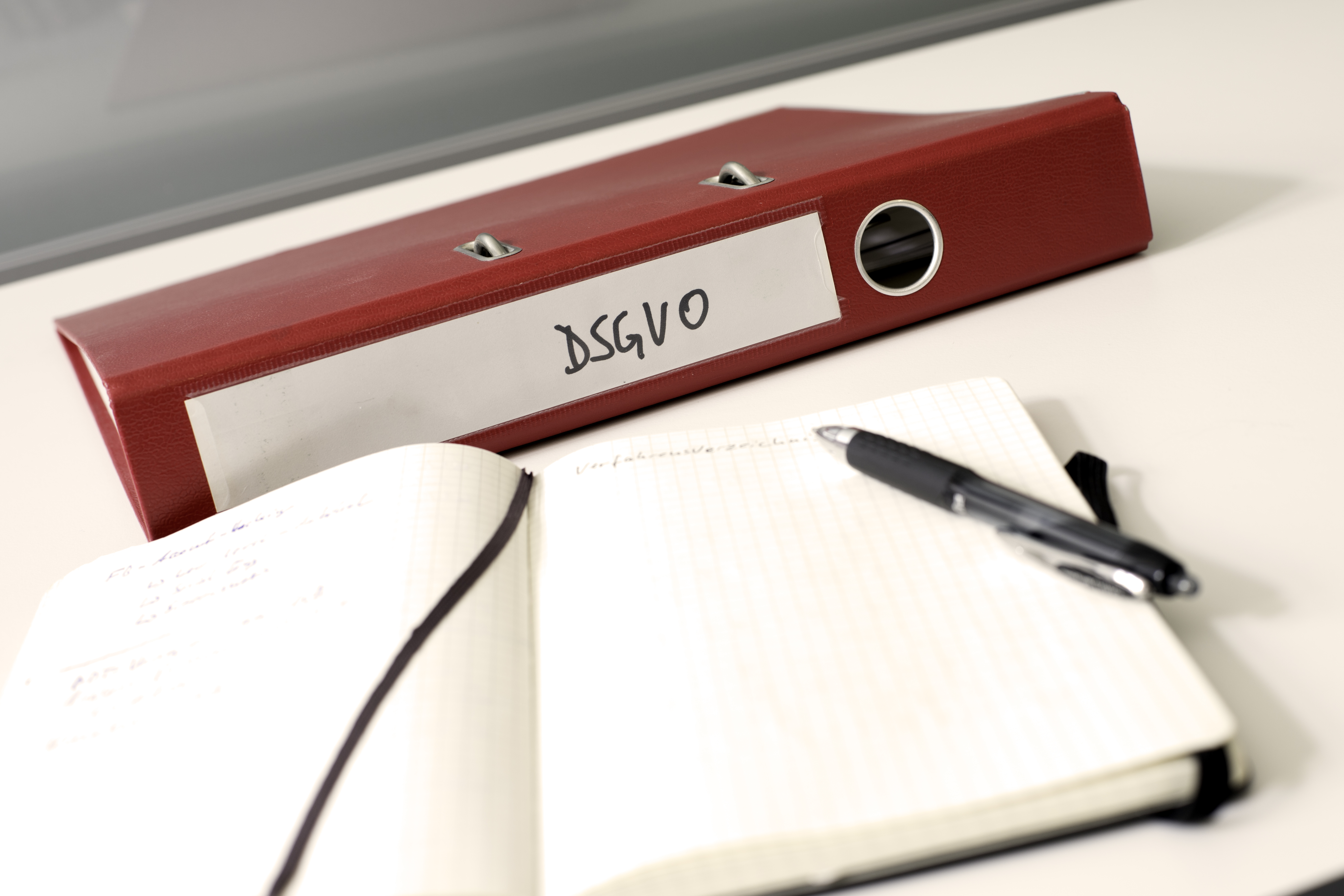 A red folder labelled ‘GDPR’. In front of it, an open notebook with a pen. The pages are blank.
